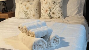 A neatly made bed with rolled towels, floral pillows, and a grey blanket.