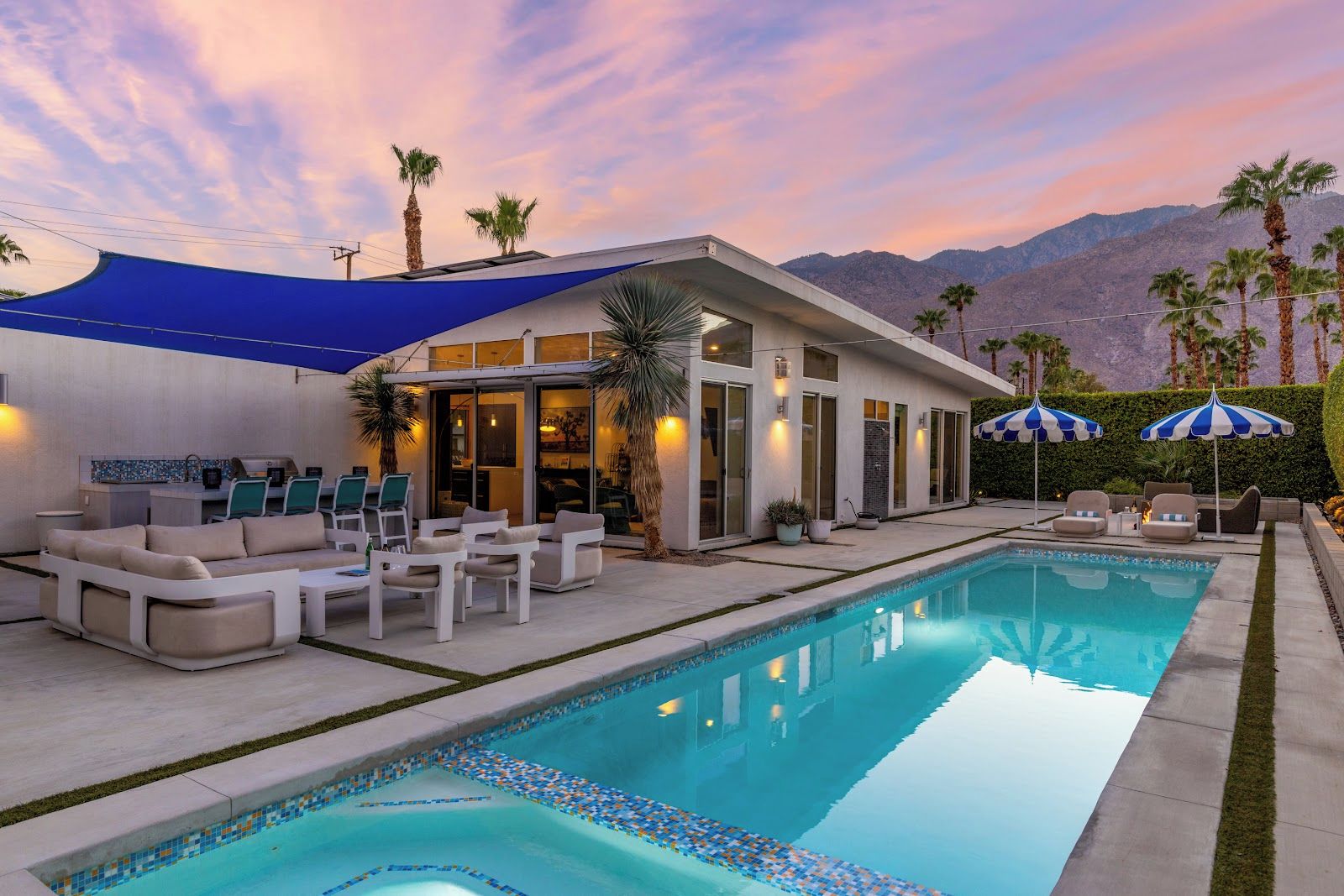 A modern outdoor pool area with a house, lounge chairs, and umbrellas.