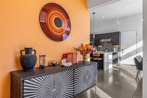 A modern kitchen with a central island, a decorative wall piece, and a vase with flowers on a console table. - Modern Desert Oasis – Luxury Retreat (Palm Springs)