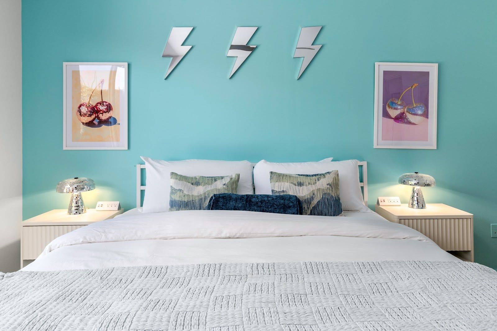 Quarto com cama, duas mesas de cabeceira, parede decorada com três raios e duas fotos emolduradas.