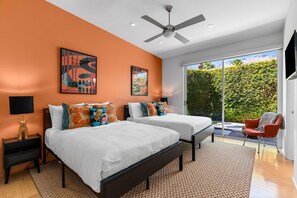 A modern bedroom with two beds, a ceiling fan, and a large window with a view of greenery. - Modern Desert Oasis – Luxury Retreat (Palm Springs)