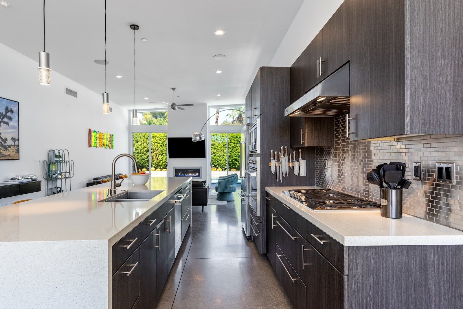 A modern kitchen with a central island, dark cabinetry, and a large window overlooking greenery.