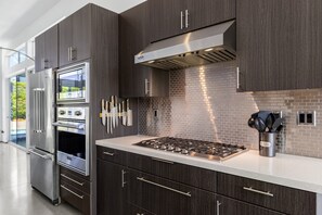 Eine moderne Küche mit dunklen Holzausziehtüren, Edelstahlgeräten und einer gefliesten Spritzschutzwand.