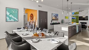 A modern kitchen with a central island, a dining area with a long table, and a kitchen island with a built-in oven. - Modern Desert Oasis – Luxury Retreat (Palm Springs)