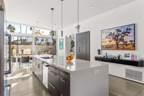 A modern kitchen with a large island, dark cabinetry, and a desert-themed painting. - Modern Desert Oasis – Luxury Retreat (Palm Springs)