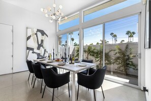 A modern dining area with a large window, a contemporary chandelier, and a minimalist table setting. - Modern Desert Oasis – Luxury Retreat (Palm Springs)