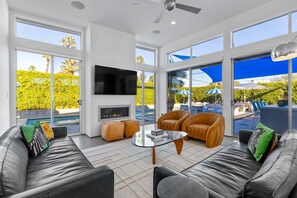 A modern living room with leather sofas, a glass coffee table, a flat-screen TV, and a fireplace. - Modern Desert Oasis – Luxury Retreat (Palm Springs)