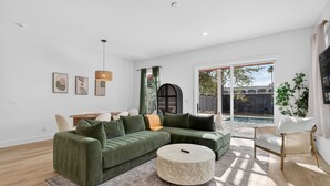 A modern living room with a sectional sofa, a round coffee table, and a large window offering a view of a backyard. - Private Pool! Game Room! 3BR Townhome Nr Downtown (St. Augustine)