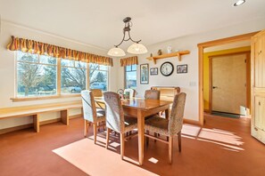 A dining room with a wooden table and chairs, a bench along the window, and a clock on the wall. - Charming Two Story Home with Hot Tub (Driggs)