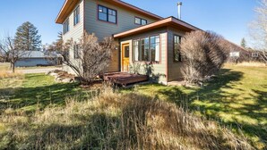 A two-story house with a front porch, a chimney, and a small yard with grass and shrubs. - Charming Two Story Home with Hot Tub (Driggs)