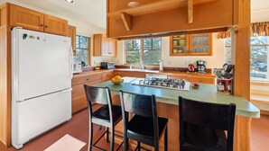A kitchen with wooden cabinets, a white refrigerator, a gas stove, and a dining area with two chairs. - Charming Two Story Home with Hot Tub (Driggs)