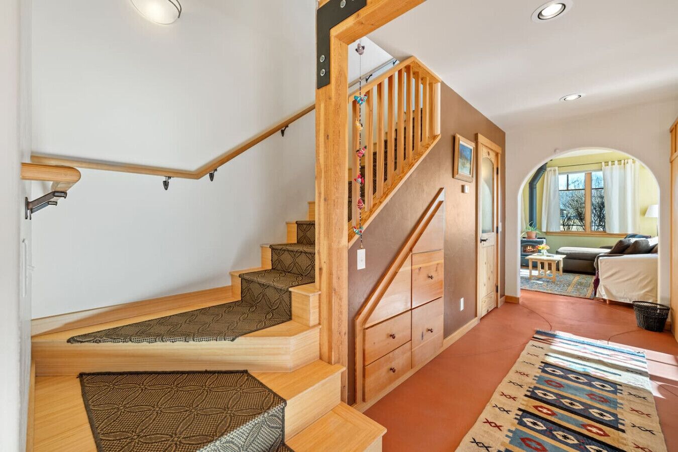 Una escalera de madera con barandilla que lleva a una habitación con un sofá y un ventanal.