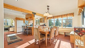 A cozy, well-lit kitchen with wooden beams, a dining area with patterned chairs, and large windows offering a view of the outdoors. - Charming Two Story Home with Hot Tub (Driggs)
