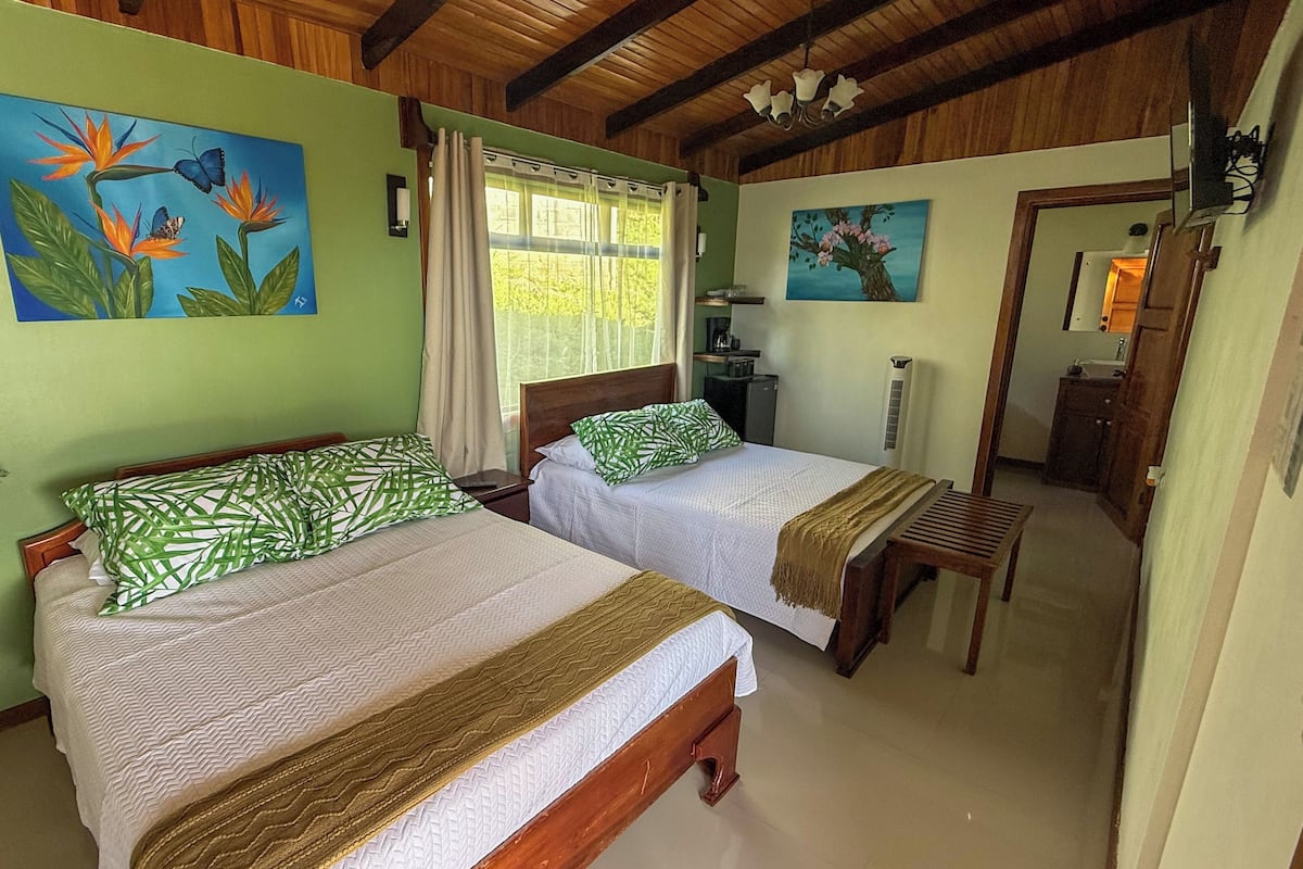 A room with two beds, green walls, wooden ceiling beams, and artwork depicting birds and flowers.