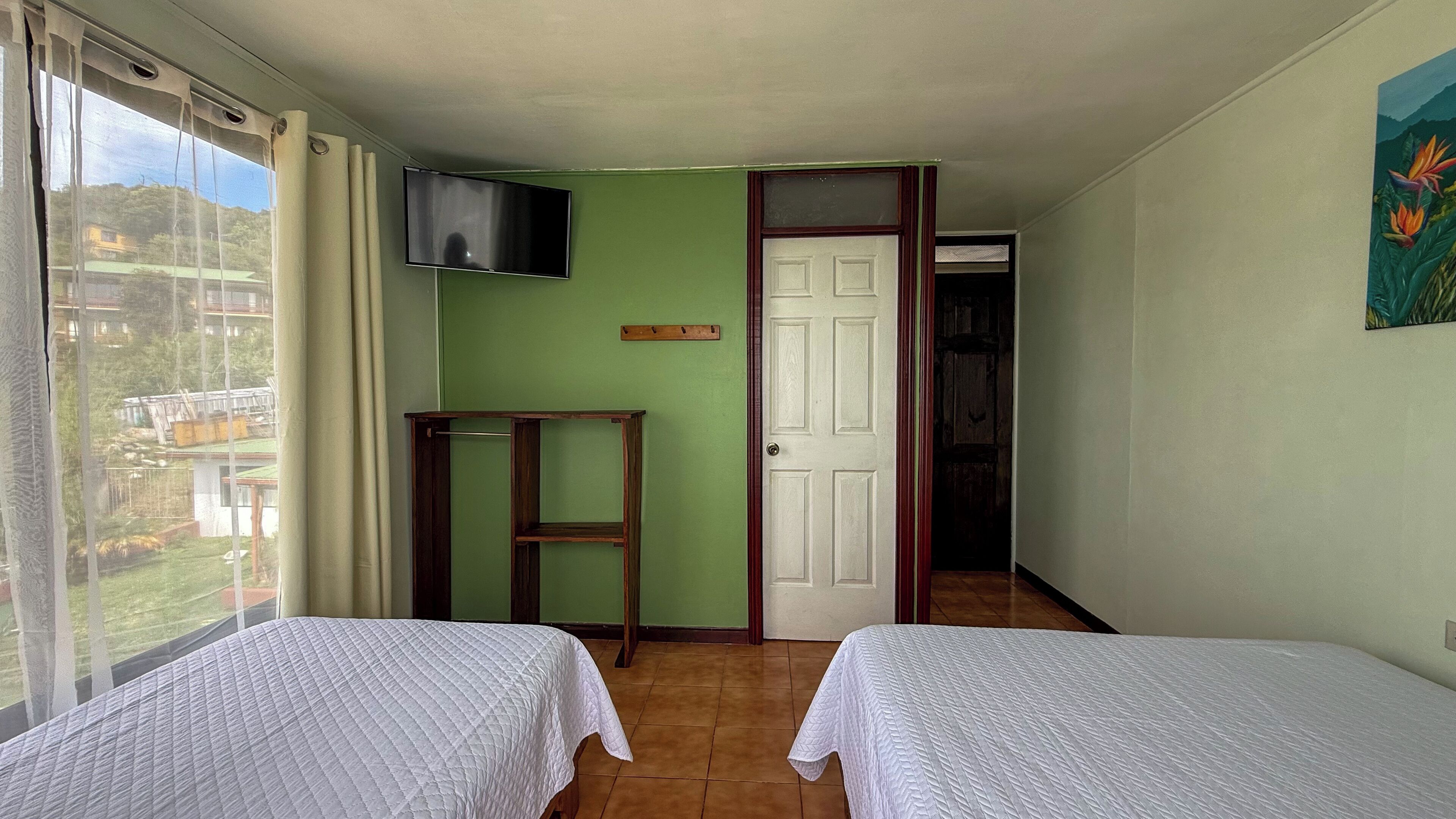 Une chambre avec deux lits, un téléviseur fixé au mur et une porte donnant sur une autre pièce.