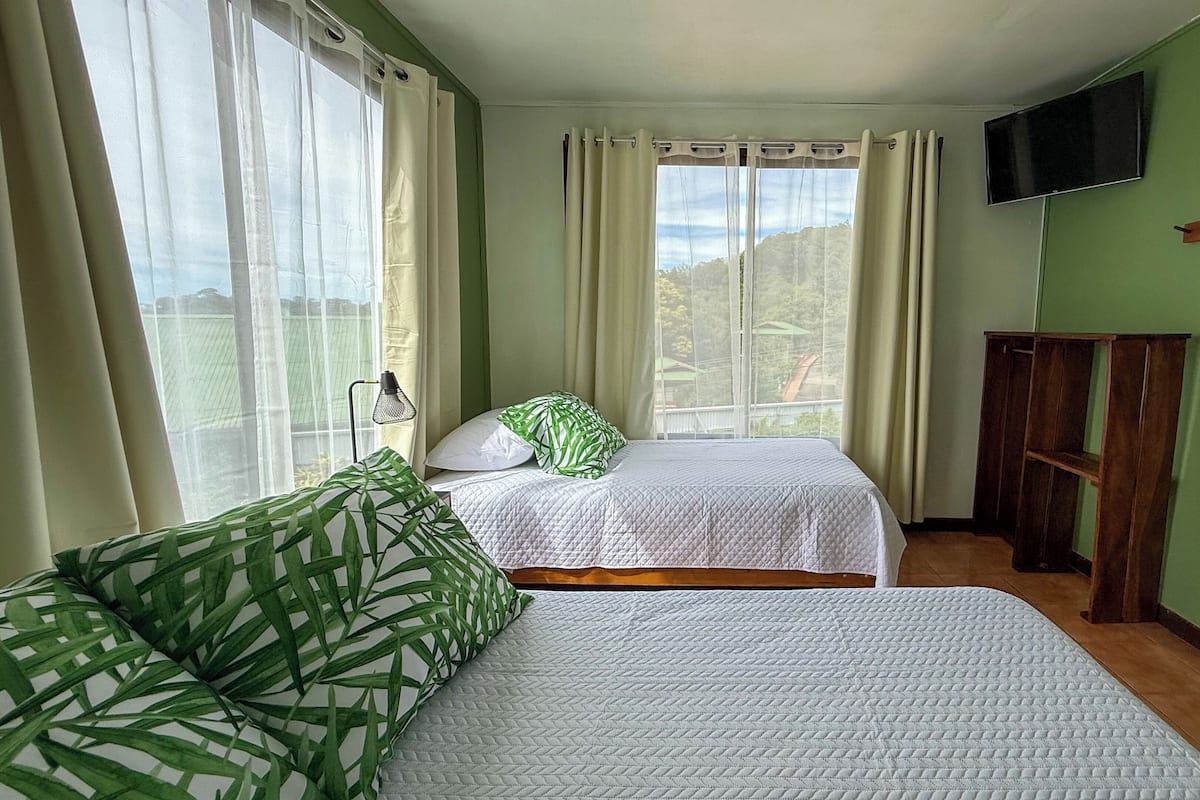 A room with two beds, a TV on the wall, and a window with curtains.