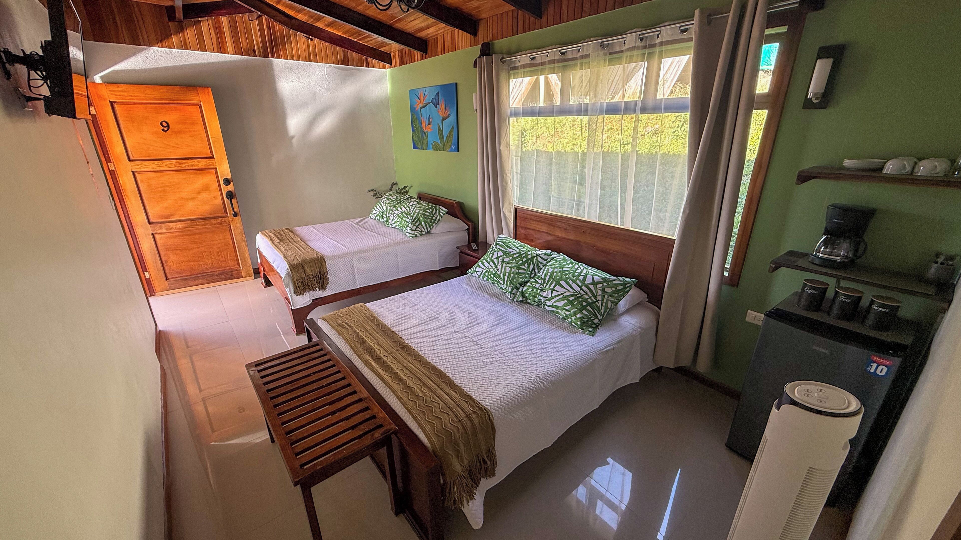 A room with two beds, a wooden wardrobe, a coffee machine, and a window with curtains.