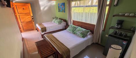 Une chambre avec deux lits, une armoire en bois, une machine à café et une fenêtre avec des rideaux.