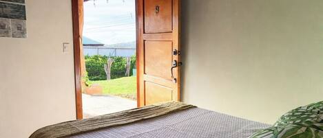 A bedroom with a bed, a wooden door, and a view of greenery outside.