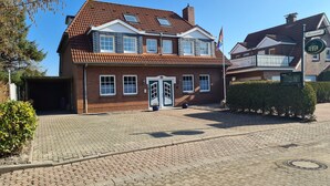 A two-story brick house with a tiled roof, a garage, and a paved driveway. - Hotel Pension Friesenruh (Esens)