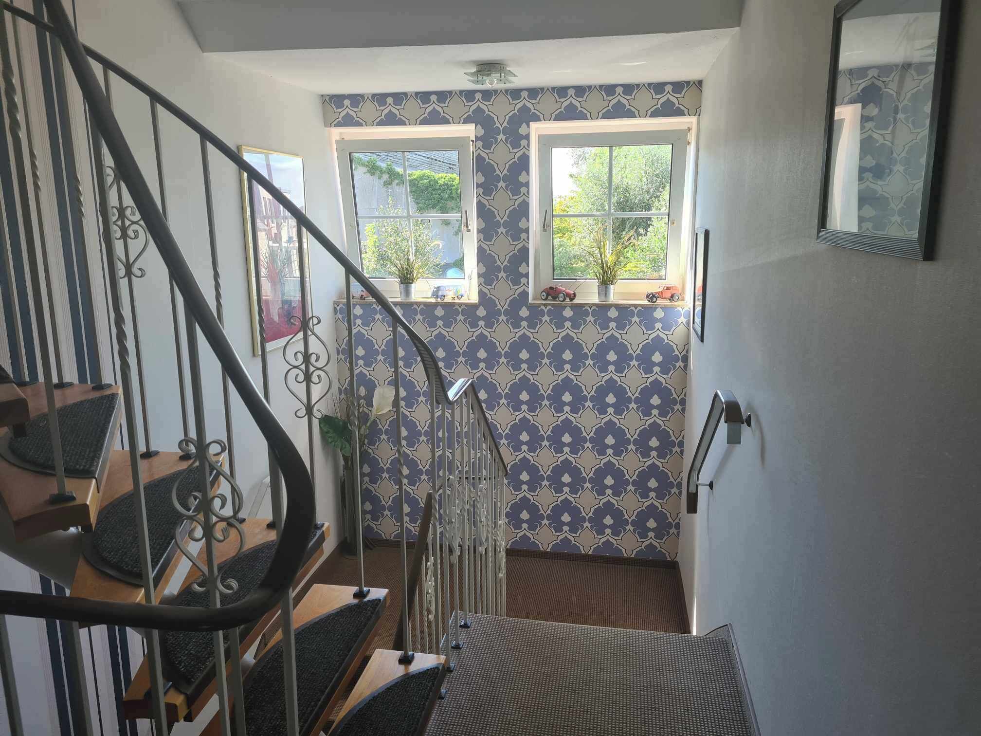 Uma escadaria com guarda-mão de metal leva a um patamar. Há duas janelas no patamar, cada uma com uma planta no parapeito.