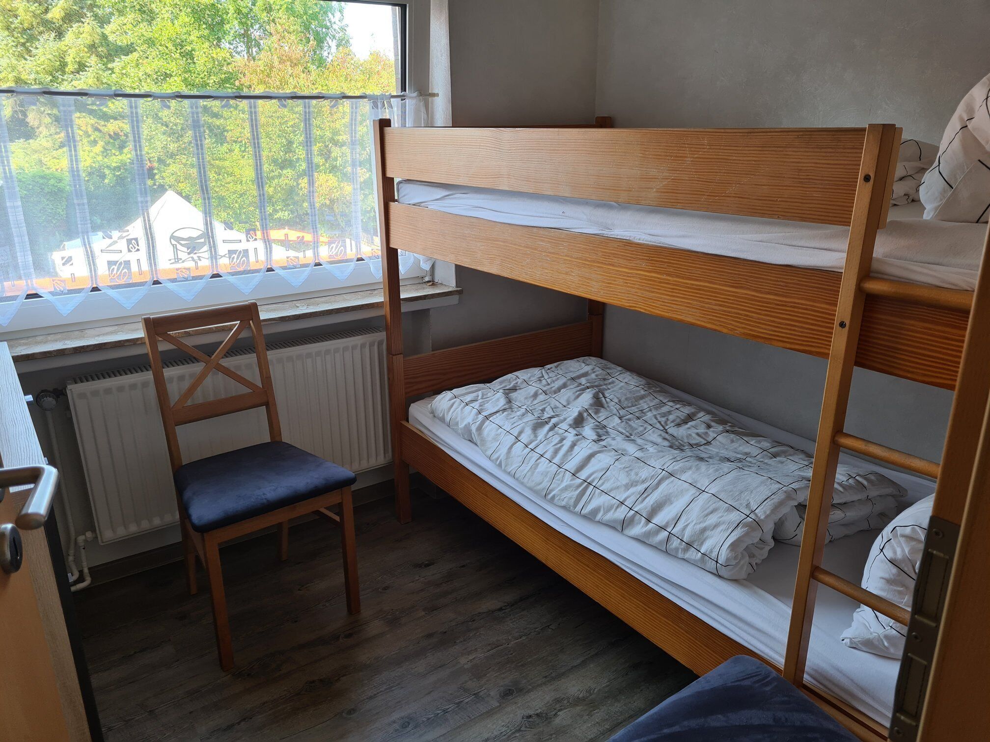 Een slaapkamer met een stapelbed, een houten stoel en uitzicht op buiten.