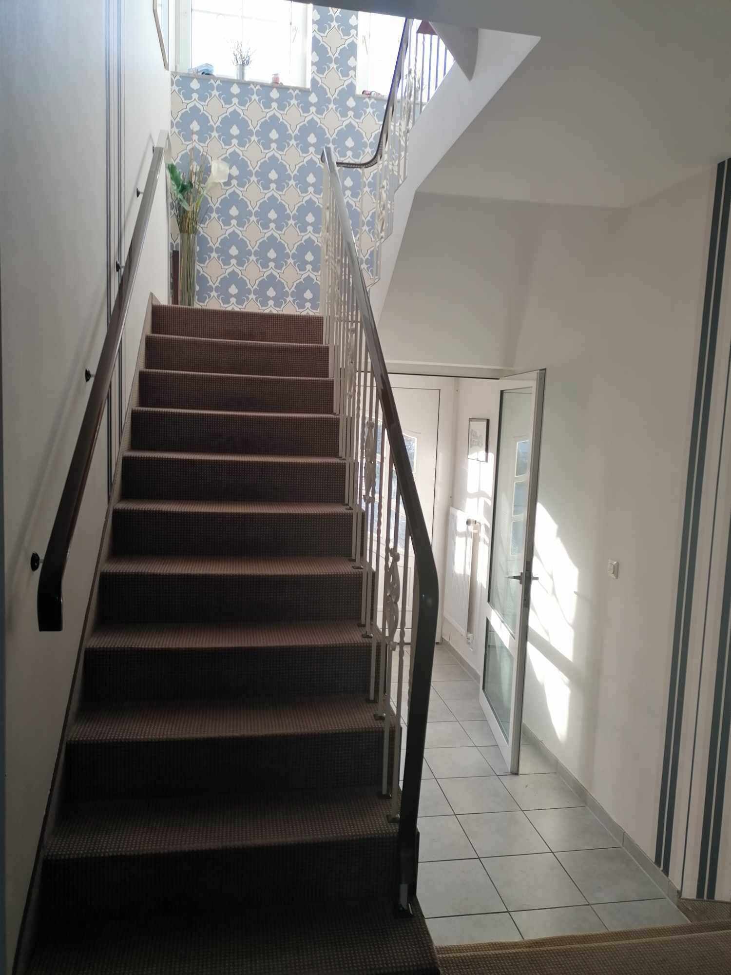 Un escalier avec une rampe en métal menant à un palier orné d’un mur à motifs et surmonté d’une porte.