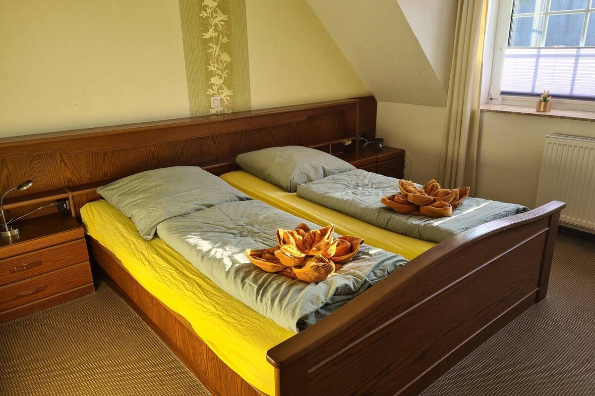 Cama doble con cabecera de madera, dos mesitas de noche y una ventana con persianas.