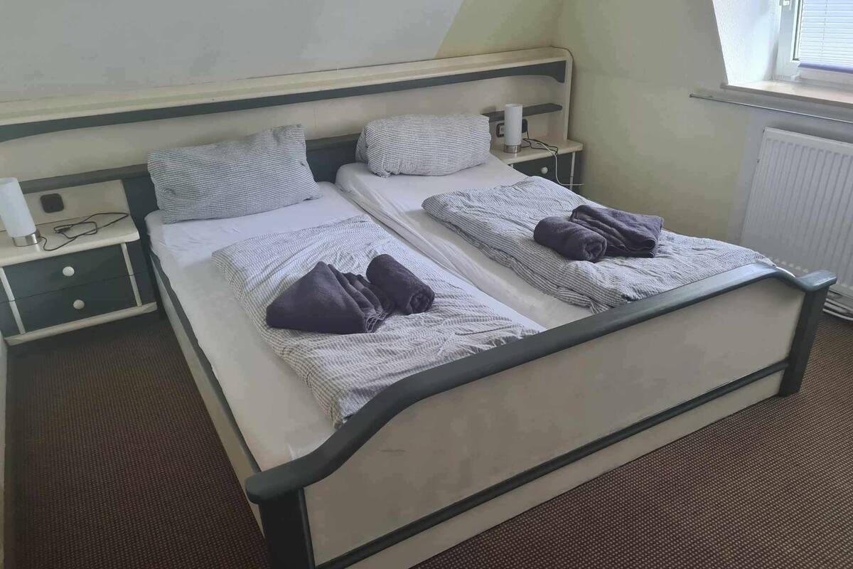 Una cama de matrimonio con dos mesitas de noche, una ventana y un radiador.
