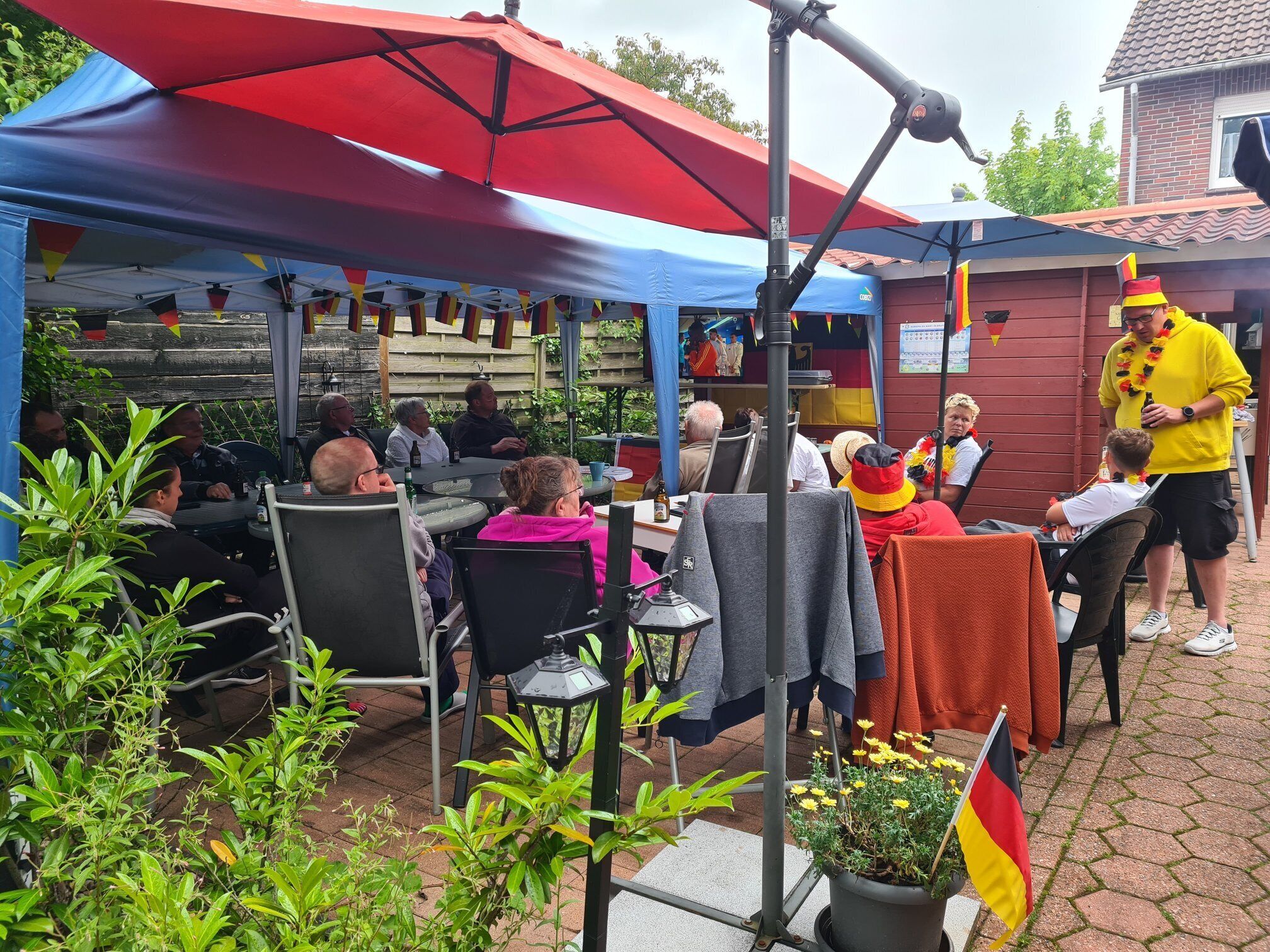 An outdoor seating area with tables and chairs under umbrellas, surrounded by greenery and potted plants.