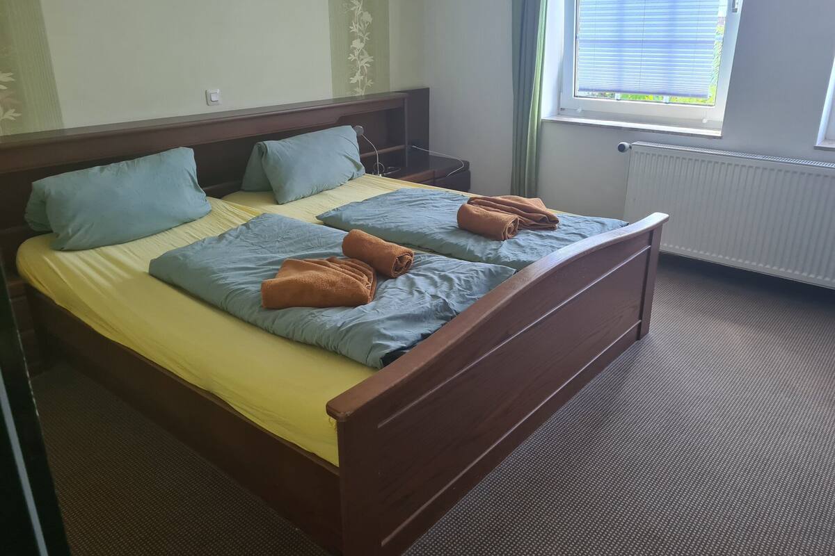 Una cama doble con cabecera de madera, dos almohadas y una toalla enrollada.