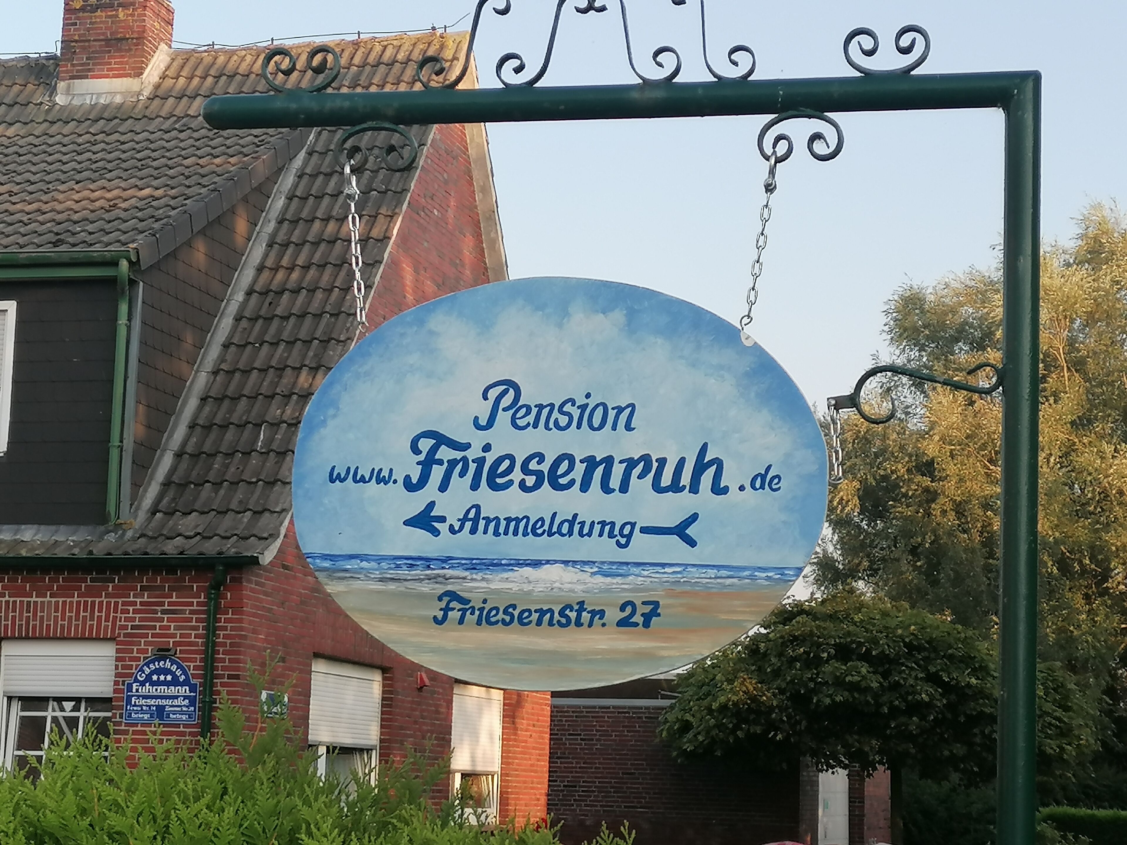 Schild für Pension Friesenruh.de mit Blick auf das Meer und einem Backsteingebäude im Hintergrund.