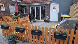 A brick house with a wooden fence, potted plants, and a barbecue grill. - Hotel Pension Friesenruh (Esens)