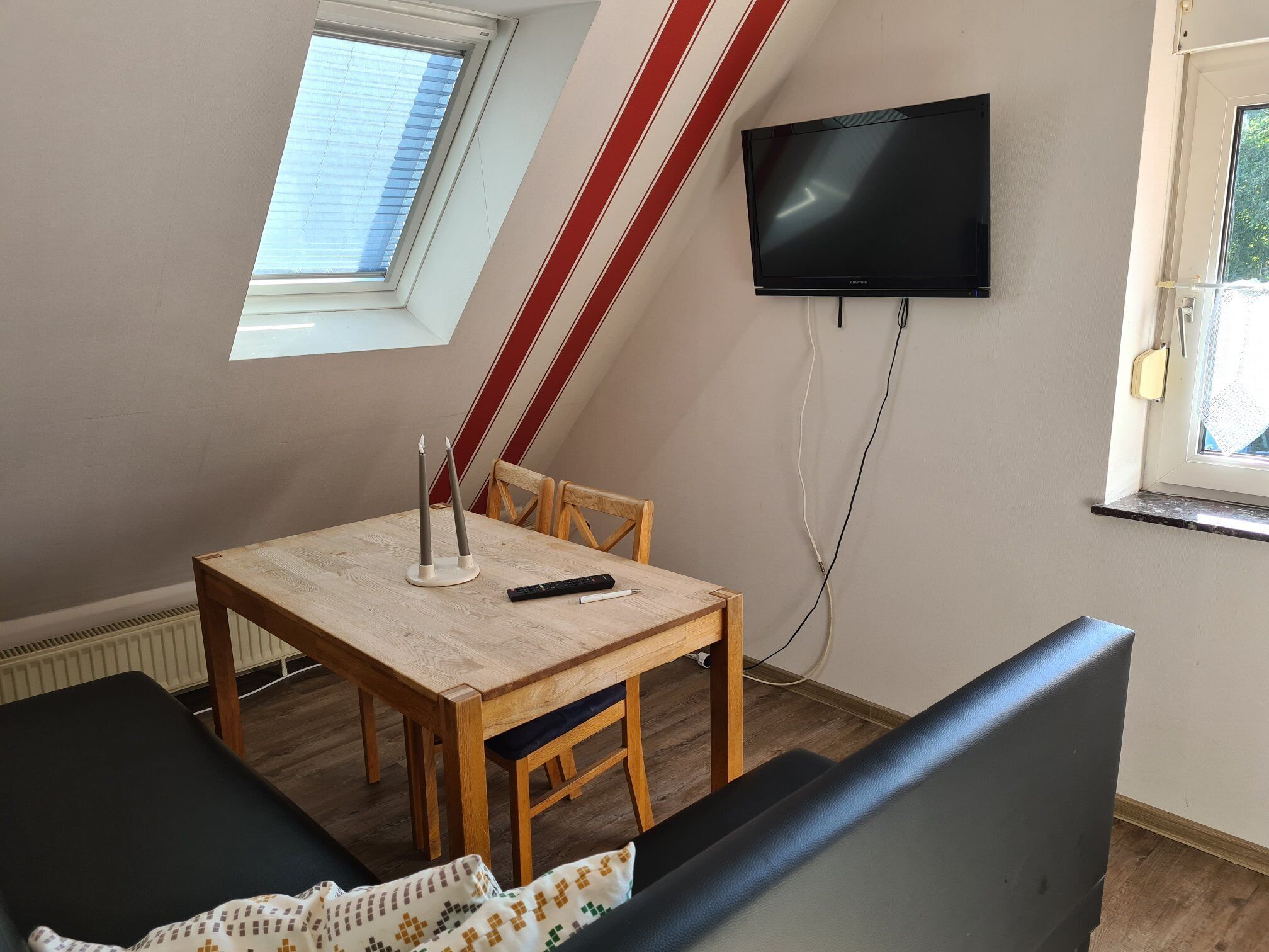 A room with a sloped ceiling, a TV mounted on the wall, a table with candles, and a sofa.