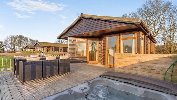 Eine Holzterrasse mit Whirlpool, Sitzgelegenheiten im Freien und einem Gebäude mit großen Fenstern.