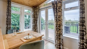 A dining area with a wooden table, chairs, and a view of a deck and greenery through large windows. - Field View 1 bed No Pets Walnut (Eye)