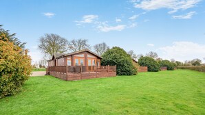 A wooden cabin with a deck, surrounded by a well-maintained lawn and trees. - Field View 2 bed (S)- Sycamore - sleeps 6 guests  in 2 bedrooms (Eye)