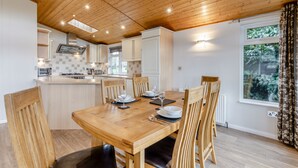 A dining area with a wooden table and chairs, a kitchen with white cabinets, and a window with curtains. - Field View 2 bed (S)- Sycamore - sleeps 6 guests  in 2 bedrooms (Eye)
