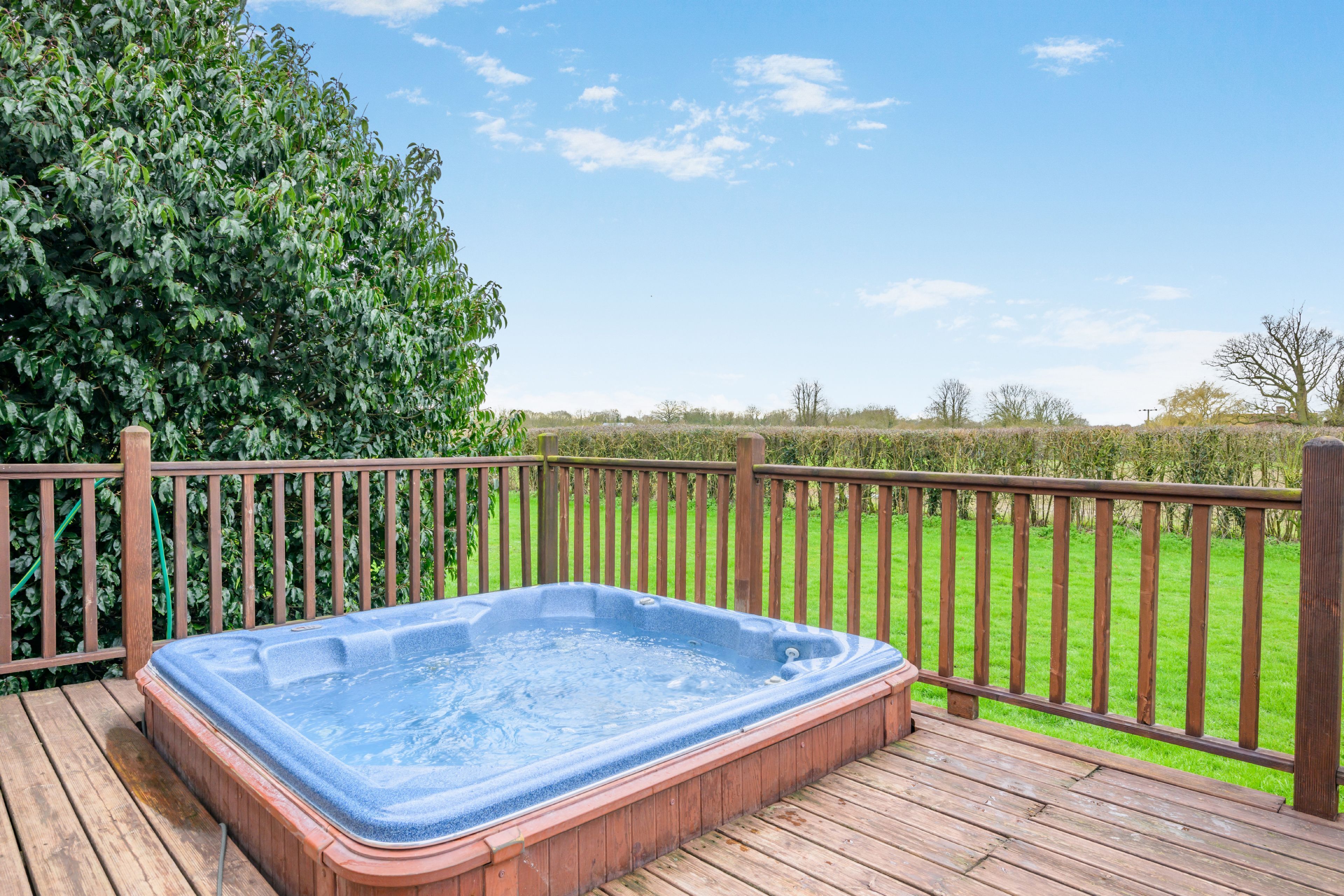 Ein Whirlpool auf einer Holzterrasse mit einem Holzzaun und einer Hecke im Hintergrund.