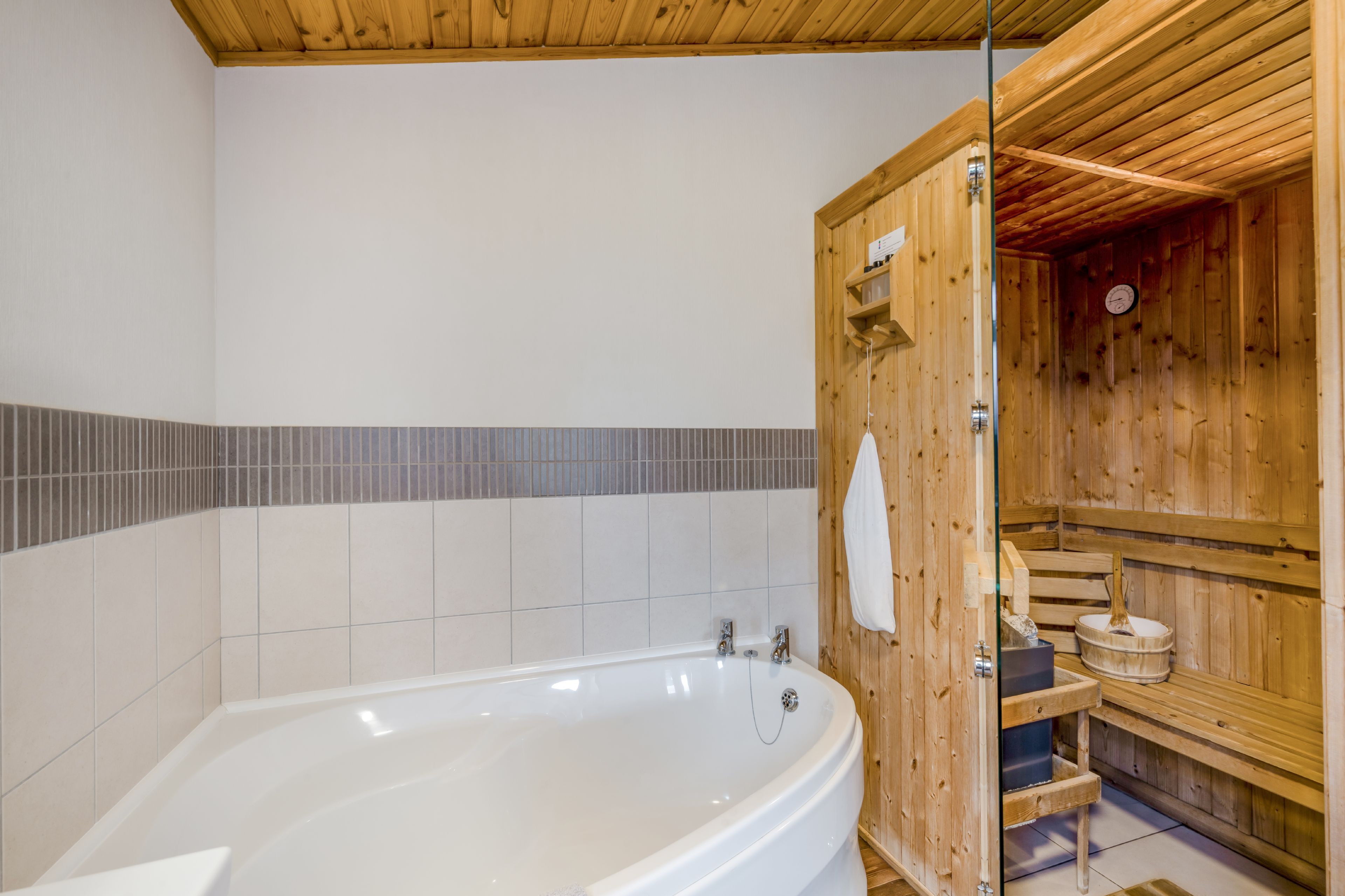Une salle de bain avec une baignoire blanche, un sauna en bois et des murs carrelés.