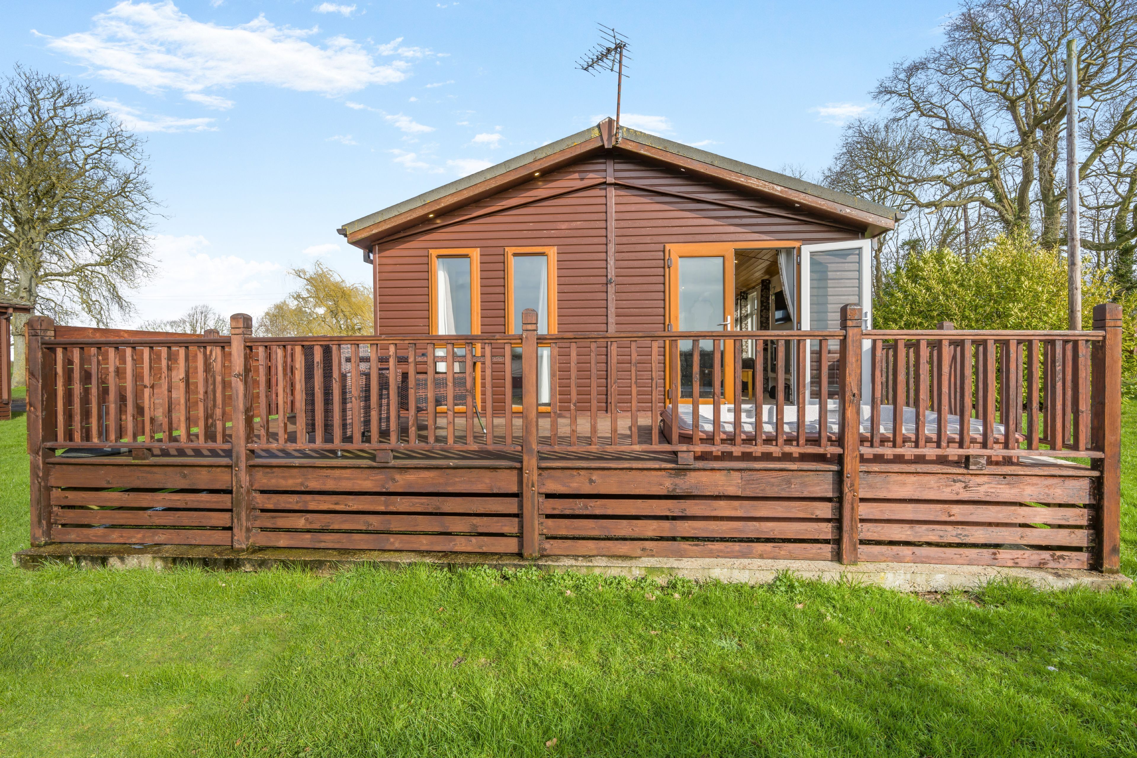 A wooden cabin with a fenced deck, large windows, and a visible door.