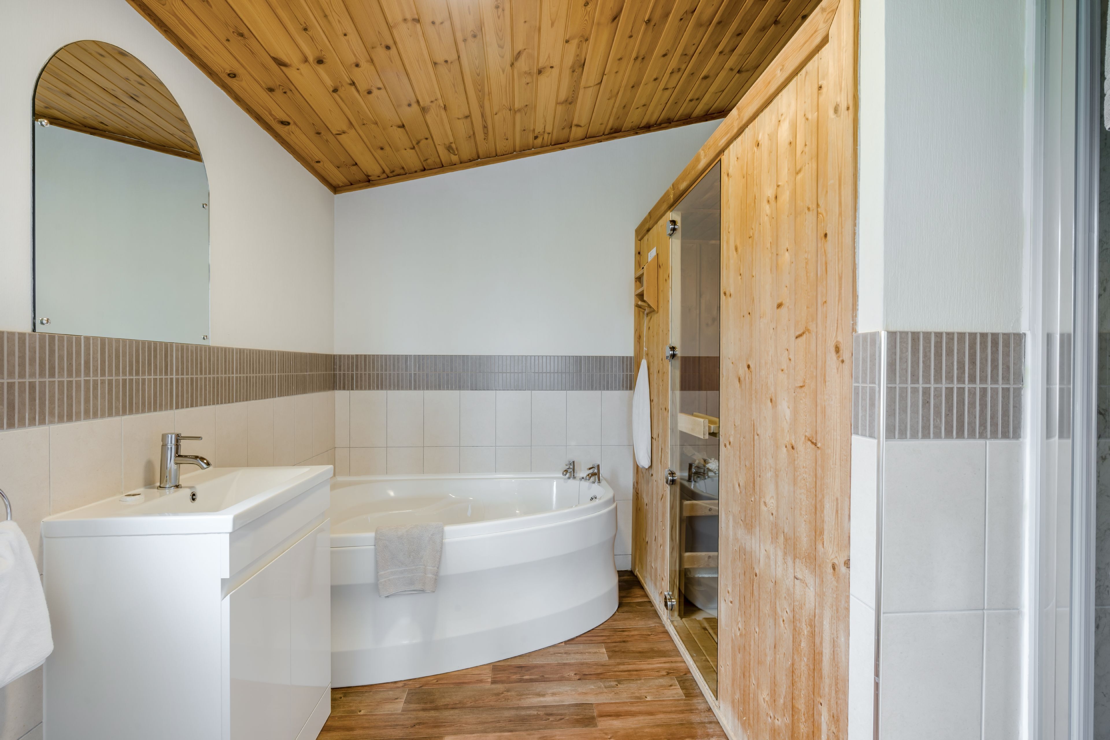 A modern bathroom with a wooden ceiling, a freestanding bathtub, a vanity with a sink, and a mirror.