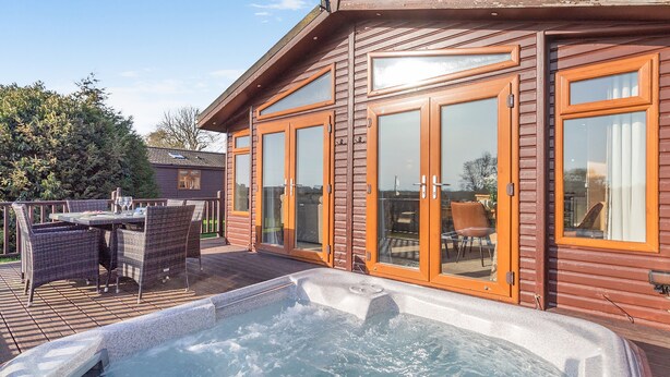 A wooden cabin with a hot tub, outdoor furniture, and large sliding glass doors. - Field View 2 bed - Hazel - sleeps 6 guests  in 2 bedrooms (Eye)