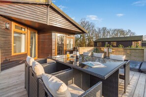 Une cabane en bois avec une table à manger en verre et des chaises en osier, un jacuzzi et une terrasse en bois.