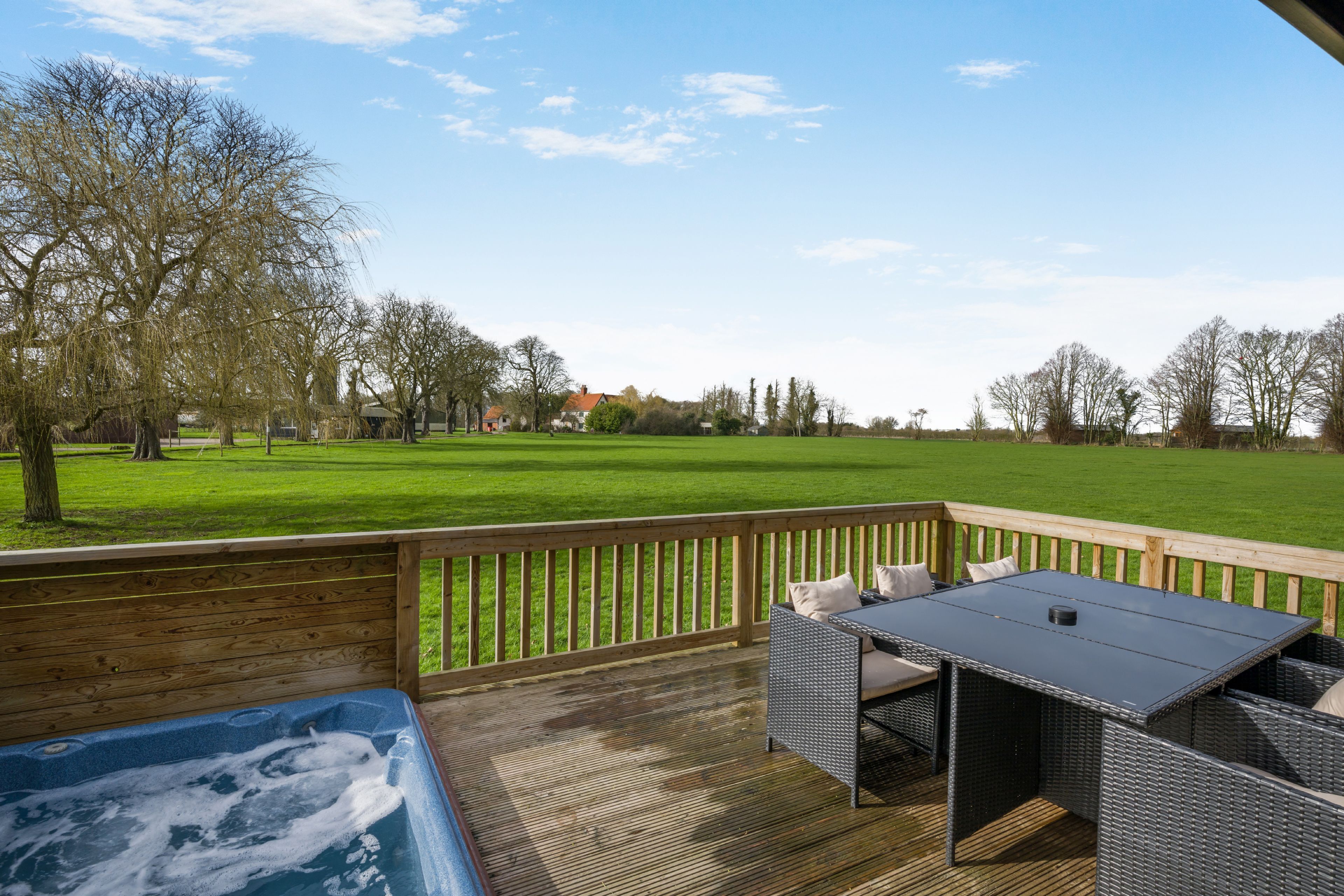 Een terras met een hottub, rieten meubels en uitzicht op een groen veld en bomen.
