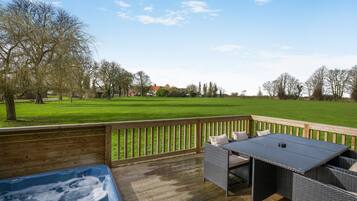 Een terras met een hottub, rieten meubels en uitzicht op een groen veld en bomen.