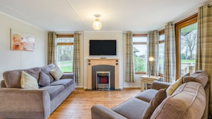 A living room with a fireplace, sofas, a television, and large windows. - Athelington Lodge - Willow  - sleeps 6 guests  in 2 bedrooms (Eye)