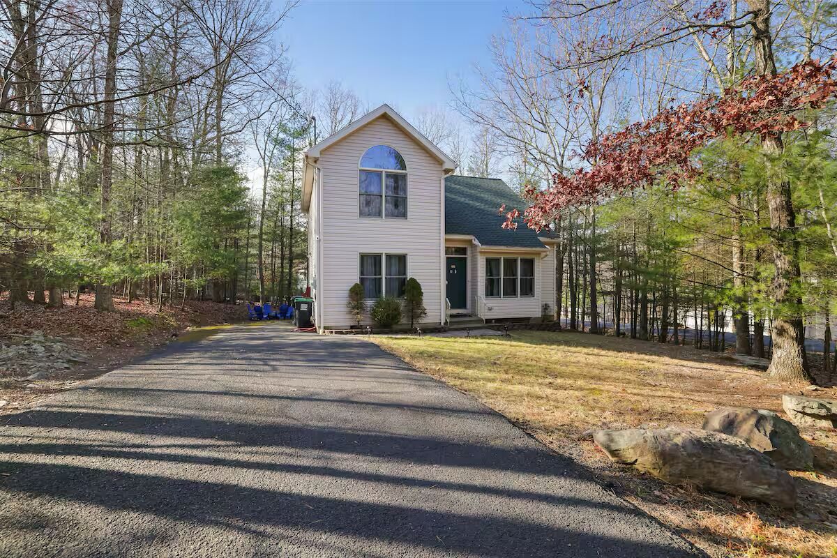 A two-story house with a front porch, surrounded by a wooded area.