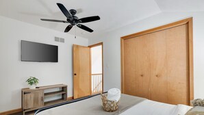 A bedroom with a bed, a ceiling fan, a TV, a wooden wardrobe, a wooden cabinet, and a wicker basket with a towel. - Modern 3BR,Game Room , FirePit& 15 mins away from Ski Resort (East Stroudsburg)