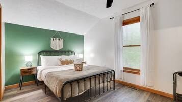 A bedroom with a bed, bedside tables, a ceiling fan, a window with curtains, and a green accent wall.